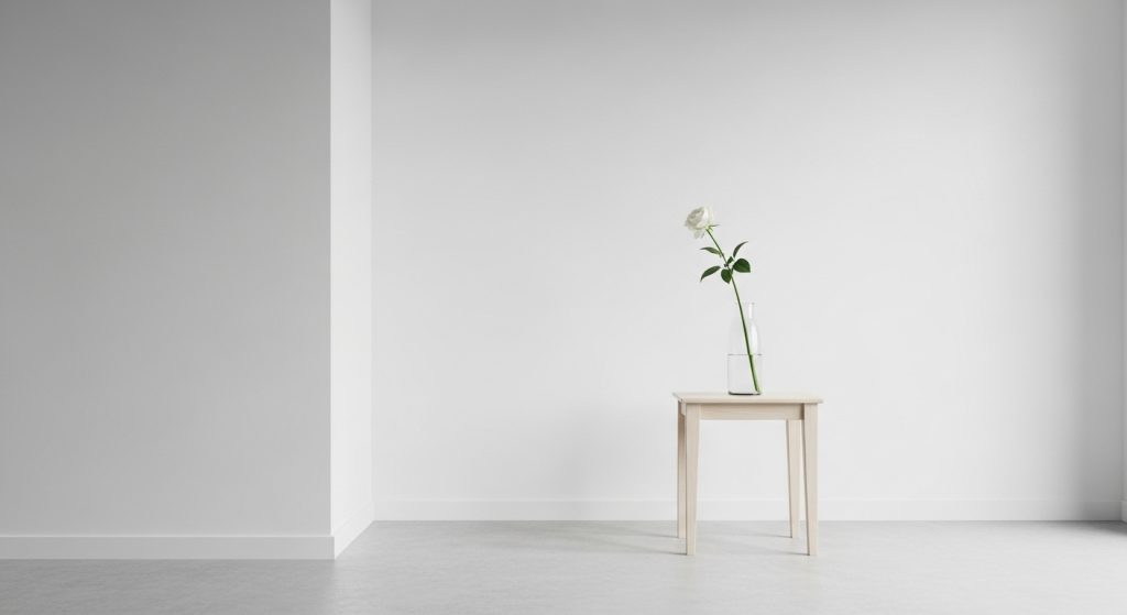 
A minimalist white room featuring a single clear vase with one white flower placed on a small side table, creating a serene and elegant aesthetic.
